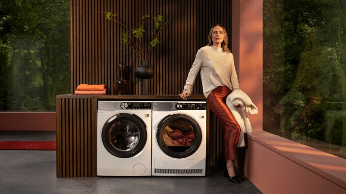 En kvinde står ved en tørretumbler og venter på, at tøjet skal blive tørt.