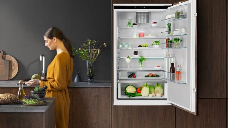 En kvinde står i et køkken med en åben køleskabsdør.