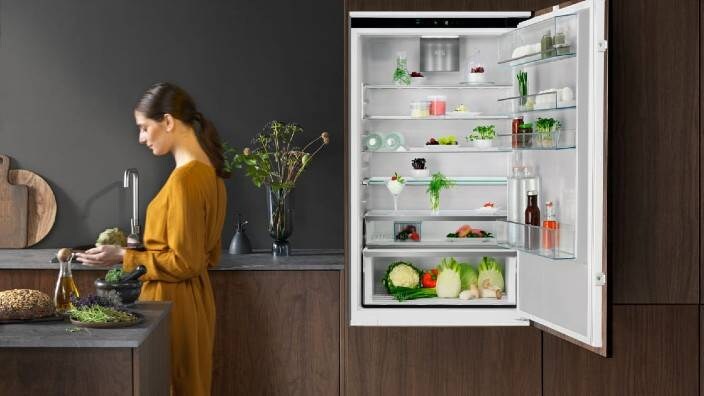 En kvinde tager noget ud af et køleskab. 