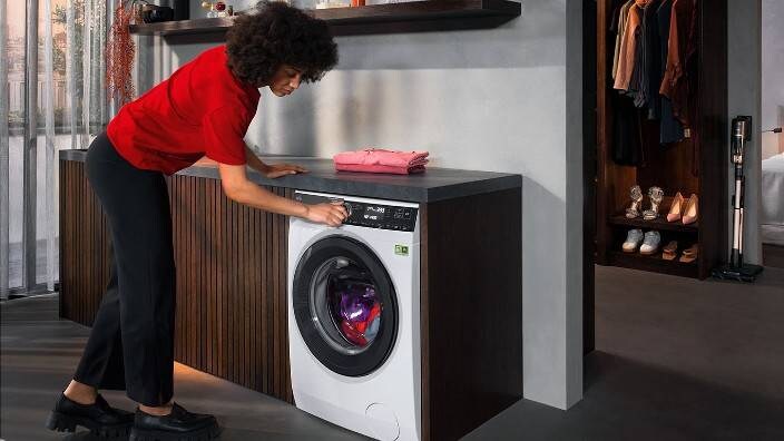 En kvinde sætter en kulørt vask over i en vaskemaskine fra AEG.