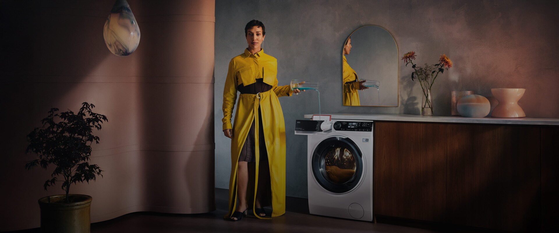 En kvinde i gul kjole hælder vaskemiddel i en vaskemaskine.